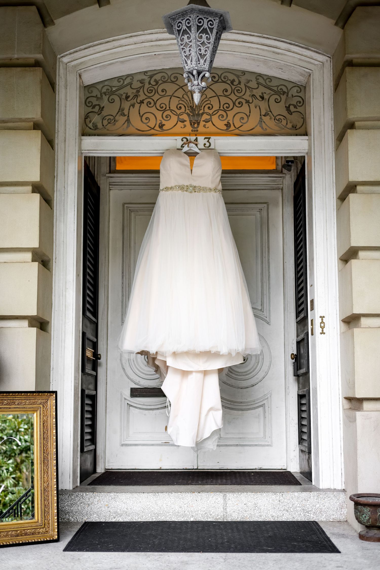 An elegant white wedding dress hangs in a doorway with ornate architectural details.