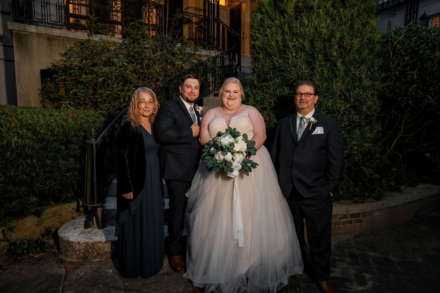 Wedding party members pose for a formal portrait against a garden backdrop.