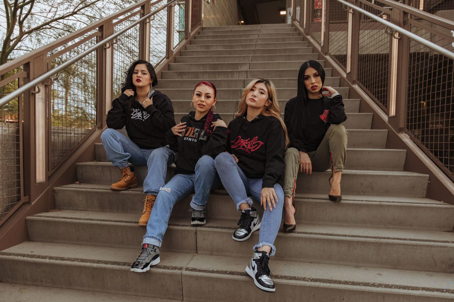 Four friends in casual wear sit together on concrete steps outdoors.