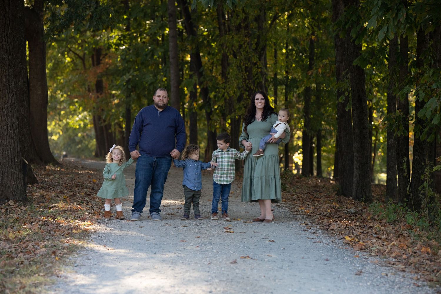 A family walking together on a tree-lined gravel path during autumn.