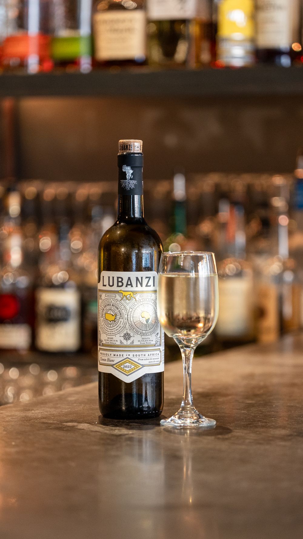 Bottle of Lubanzi wine and wine glass on wooden bar counter with blurred background.