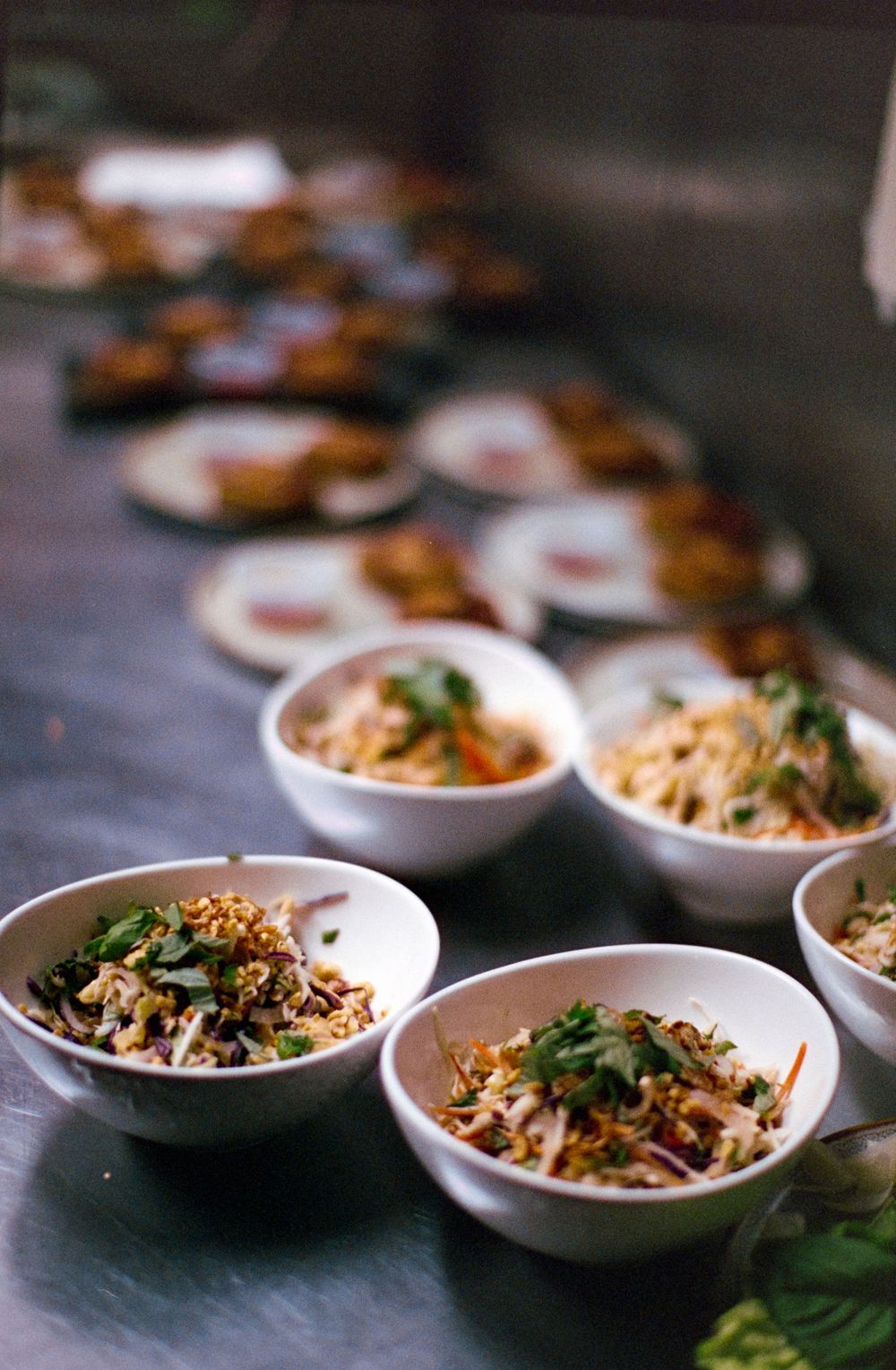 Small white bowls filled with fresh Asian noodle salad garnished with herbs and vegetables.