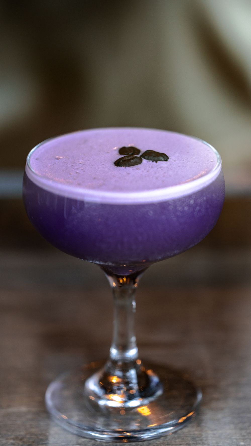 A purple cocktail garnished with coffee beans in a coupe glass.