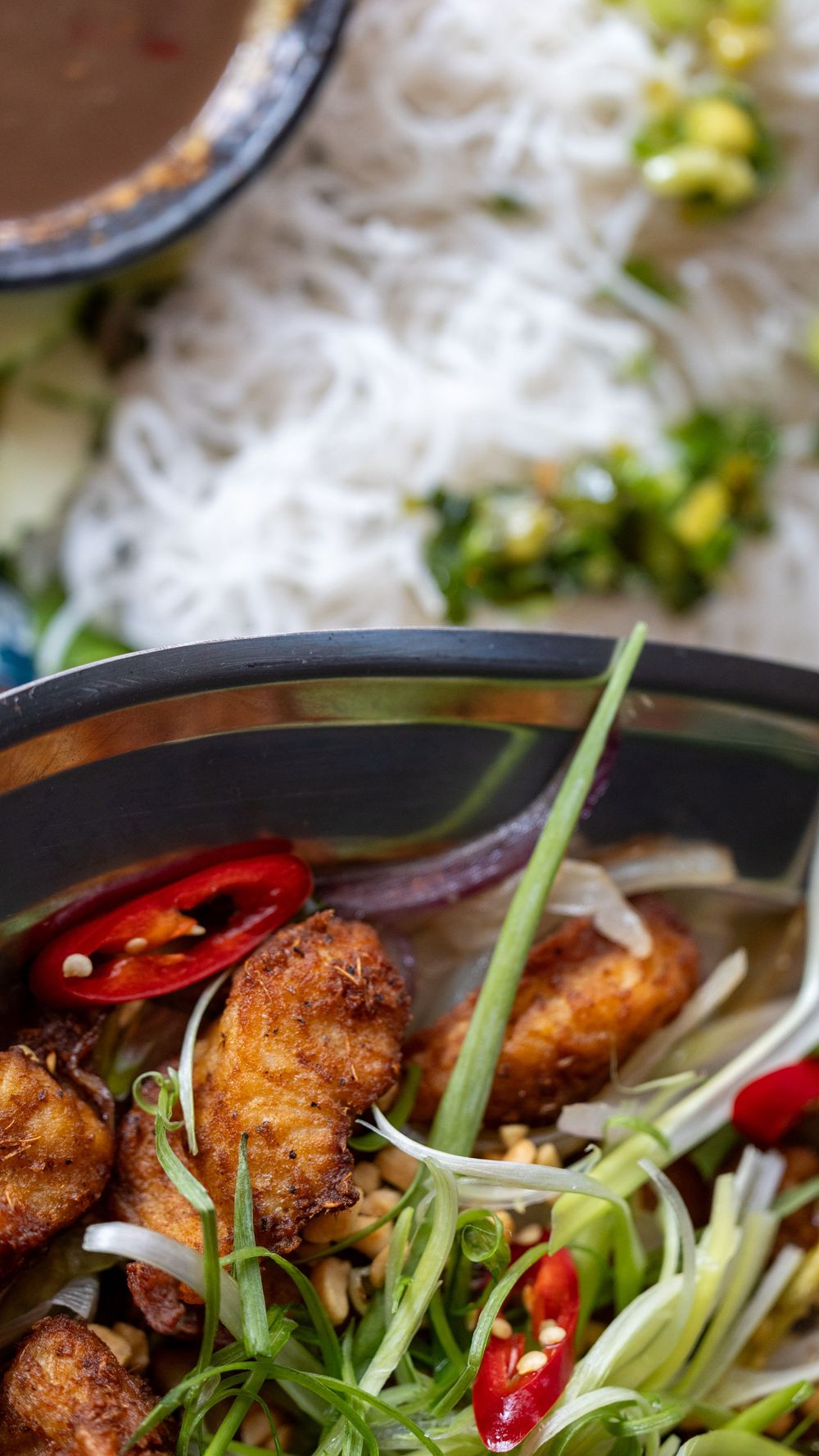 Asian soup bowl with fried meat, chili peppers, and fresh vegetables in dark broth.