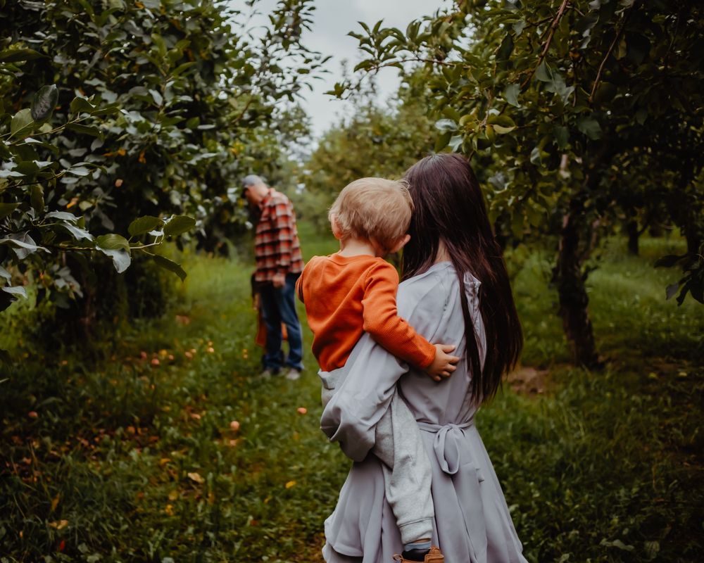 Family enjoying time together in apple orchard during autumn season.