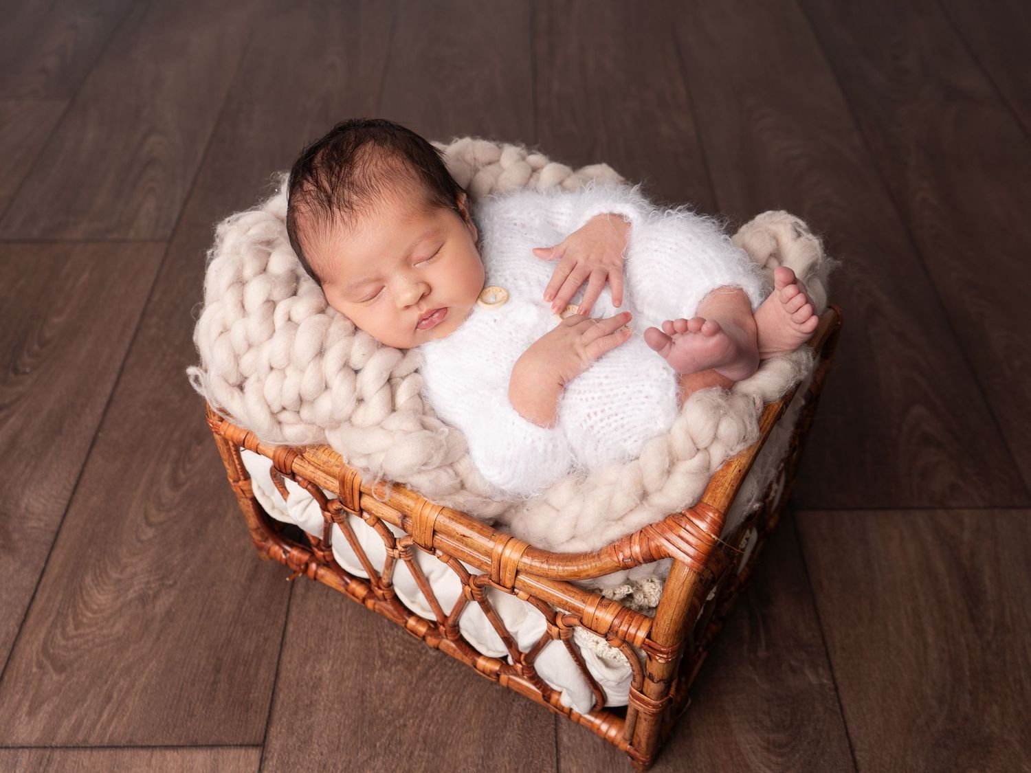 Baby girl sleeping in a basket in white fluffy onesie on a cream chunky knit blanket at newborn photoshoot in Doncaster.