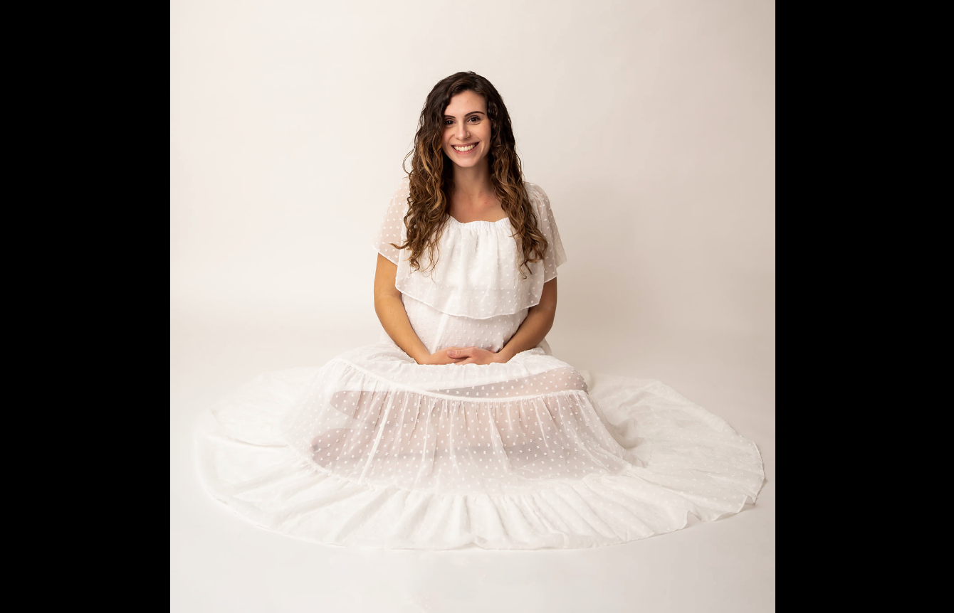 Woman in white dress sits elegantly on studio floor surrounded by flowing tulle fabric.