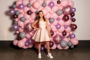Bat Mitzvah girl poses in front of a pink balloon wall - Bat Mitzvah Photography