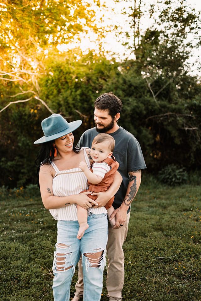Happy family with tattoos holding baby at golden hour in lush green park.