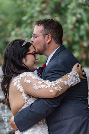 A romantic moment between newlyweds wearing wedding attire embracing and sharing a kiss in a garden setting.