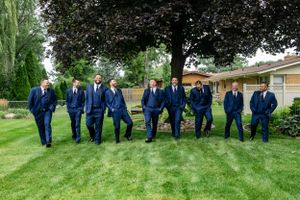 Groomsmen in navy suits pose together on a manicured lawn.