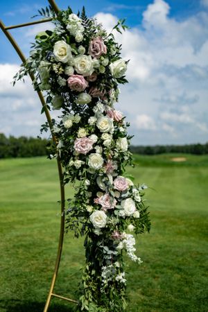 Elegant floral arch arrangement with white and pink roses against a blue sky on a golf course.