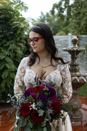 A bridal portrait in a lace wedding dress beside an ornate garden fountain.