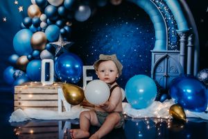 Cake smash photo setup with blue and gold balloons, wooden crates, and starry background.