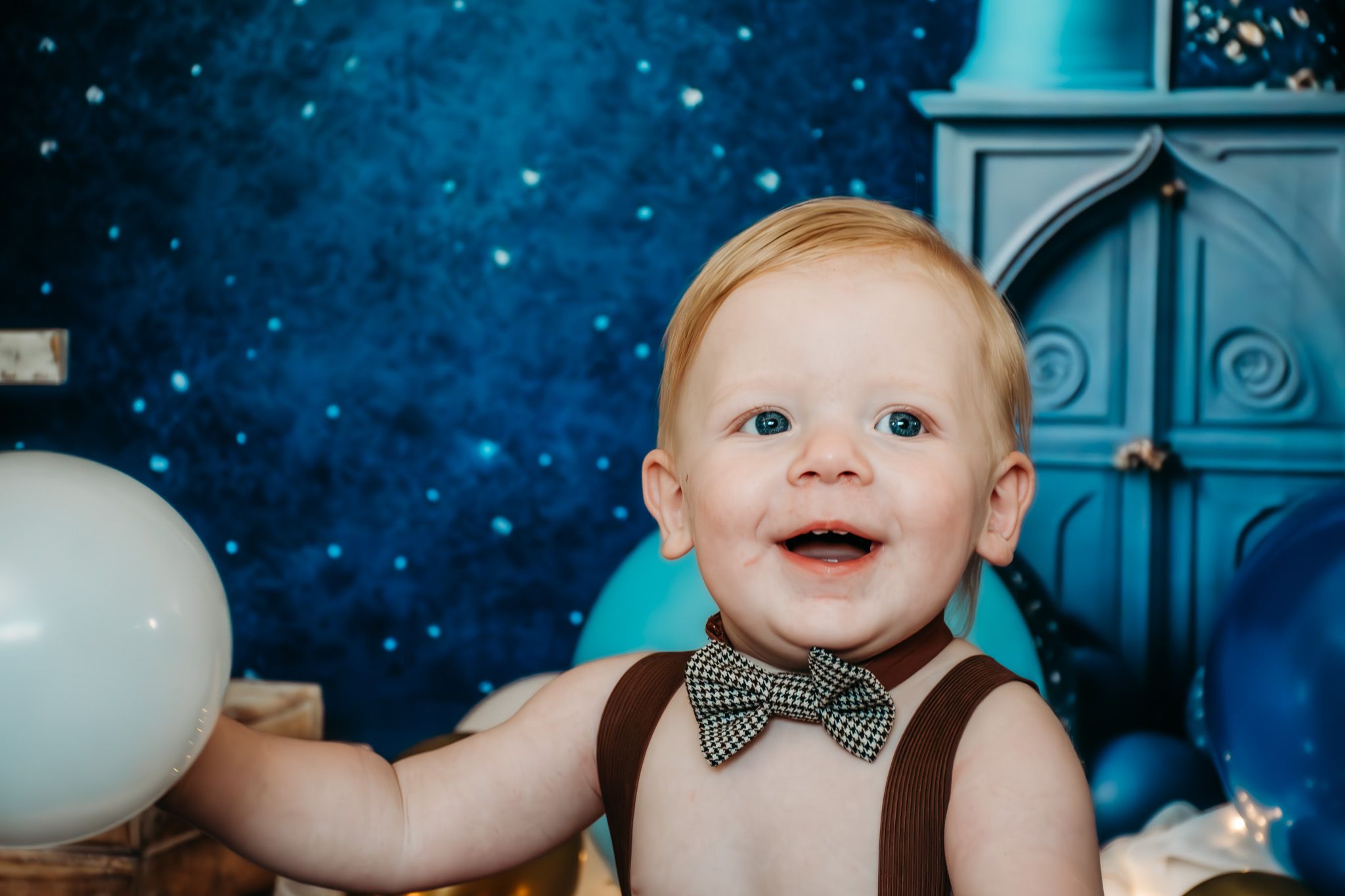 First birthday photo shoot with blue and gold balloons against a starry backdrop and decorative bow tie.