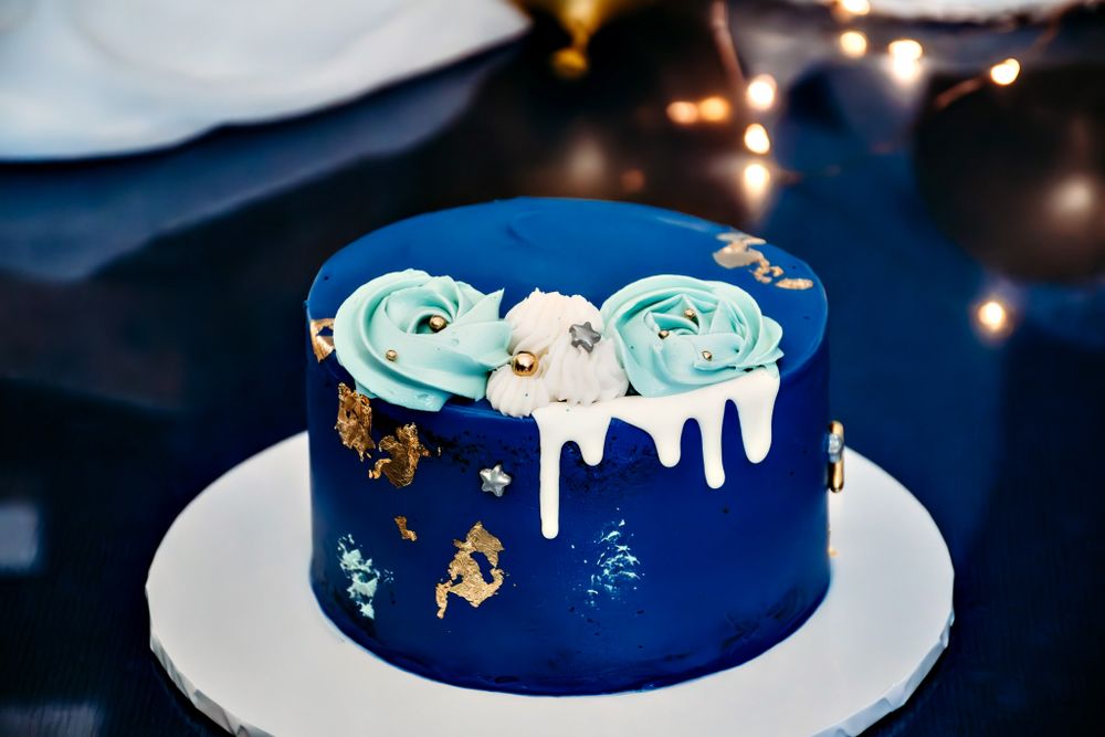 Navy blue birthday cake with gold accents and mint green decorative flowers on white cake stand.
