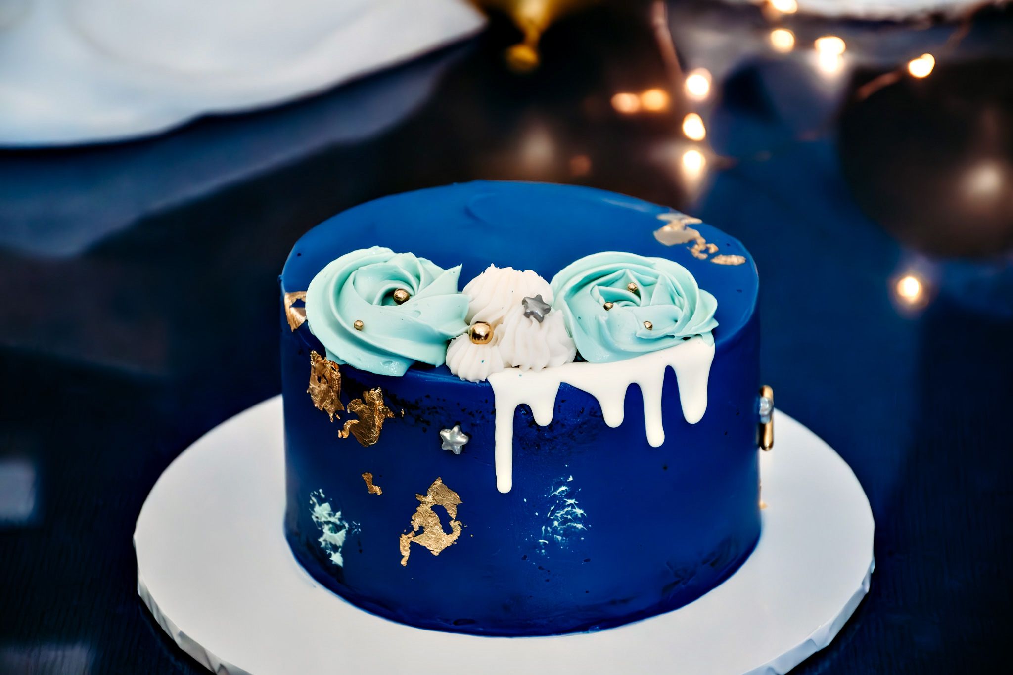 Navy blue birthday cake with gold accents and mint green decorative flowers on white cake stand.