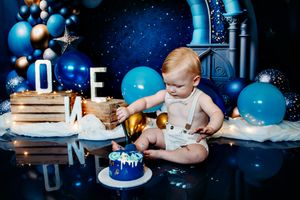 Birthday cake smash scene with blue and gold decorations against starry backdrop.