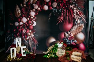 Elegant party decoration with burgundy balloons and feathers against a dark background.