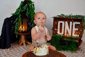 First birthday cake smash setup with woodland theme decorations and green foliage.