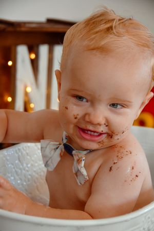 Baby covered in chocolate cake during first birthday smash cake photoshoot.