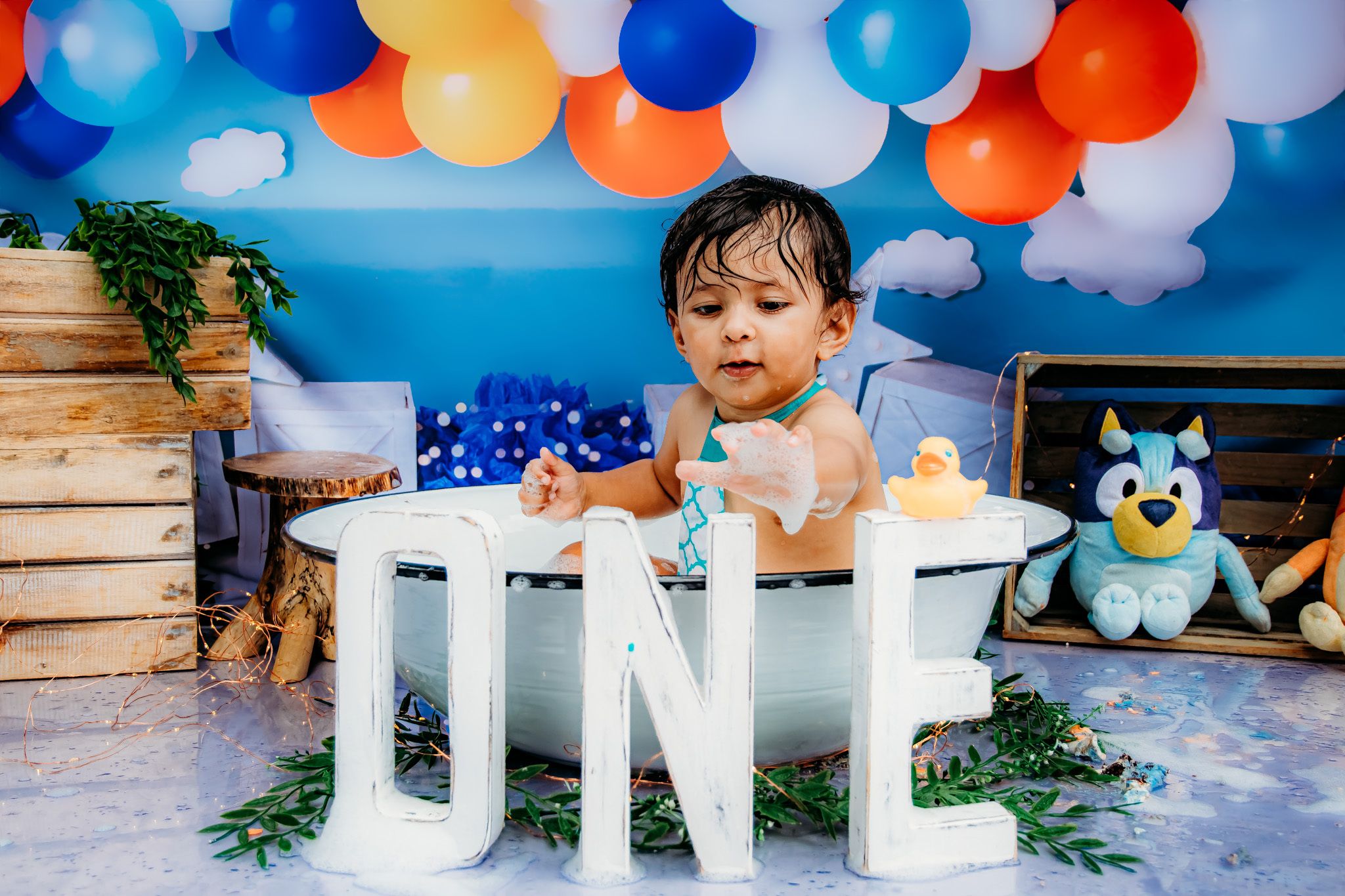 Birthday party scene with blue and orange balloon garland and decorative lettering.