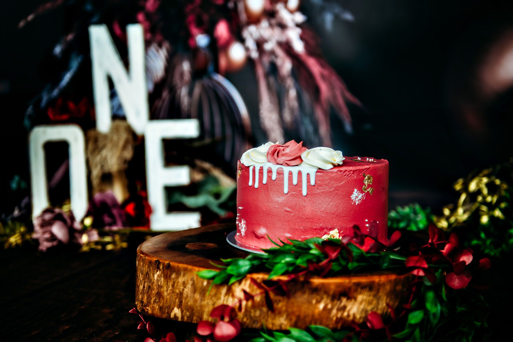 Elegant wedding cake with red and gold details displayed on a rustic wooden stand with greenery accents.