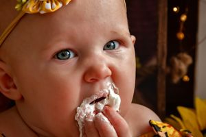 Close-up photo of a baby with frosting smeared on their face and wearing a yellow bow.