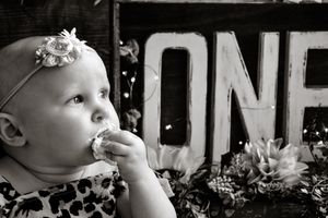 Black and white photo of a baby in a floral dress looking up with a ONE sign in background.