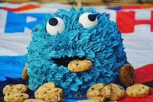 A bright blue Cookie Monster cake decorated with chocolate chip cookies on a patriotic tablecloth.