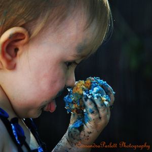 Baby with blue frosted cake on face smiles during cake smash photo session.