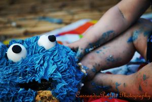 Close-up of a blue Cookie Monster cake with hands reaching for it.
