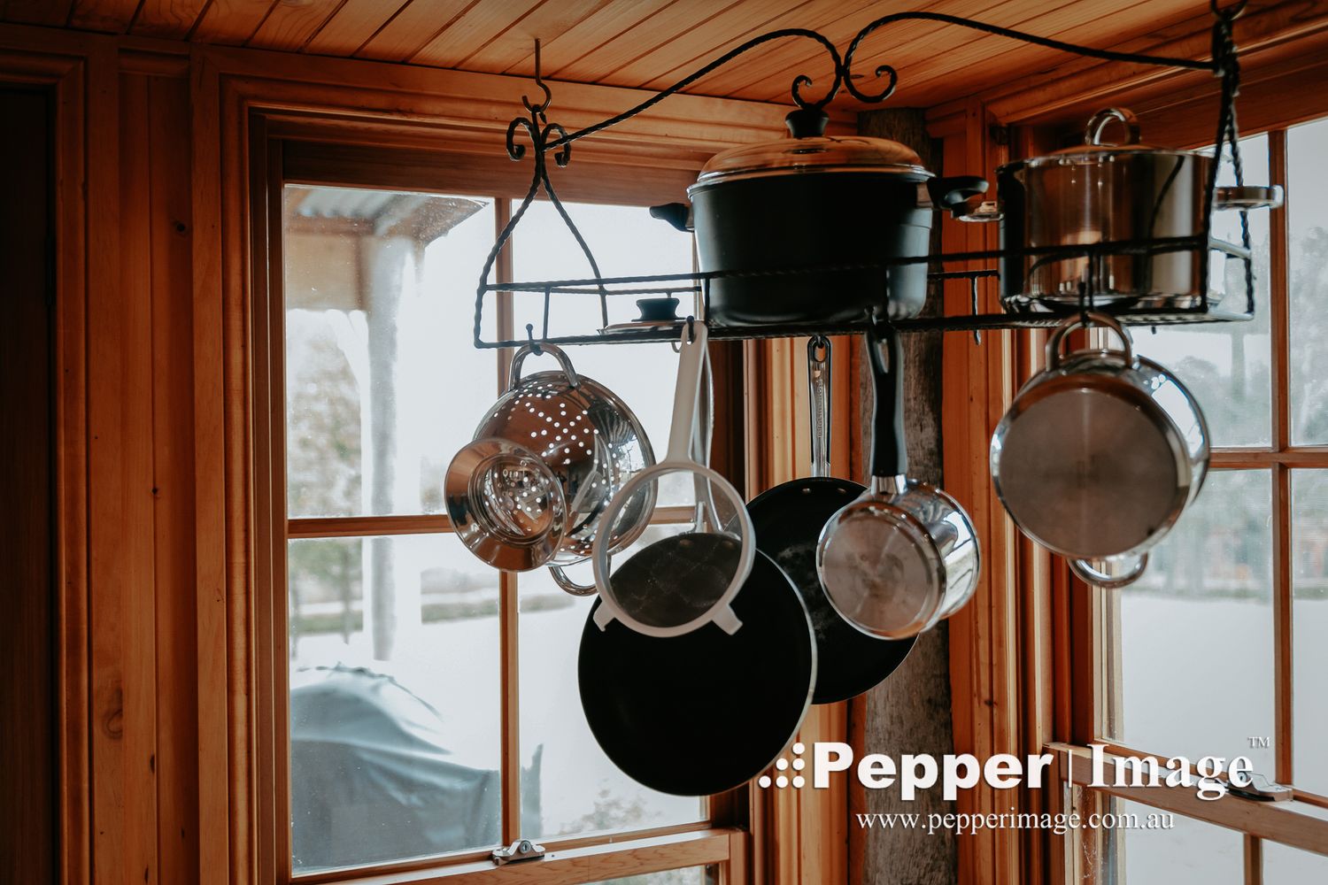Rustic kitchen pot rack with hanging pots and pans in front of a wooden framed window.