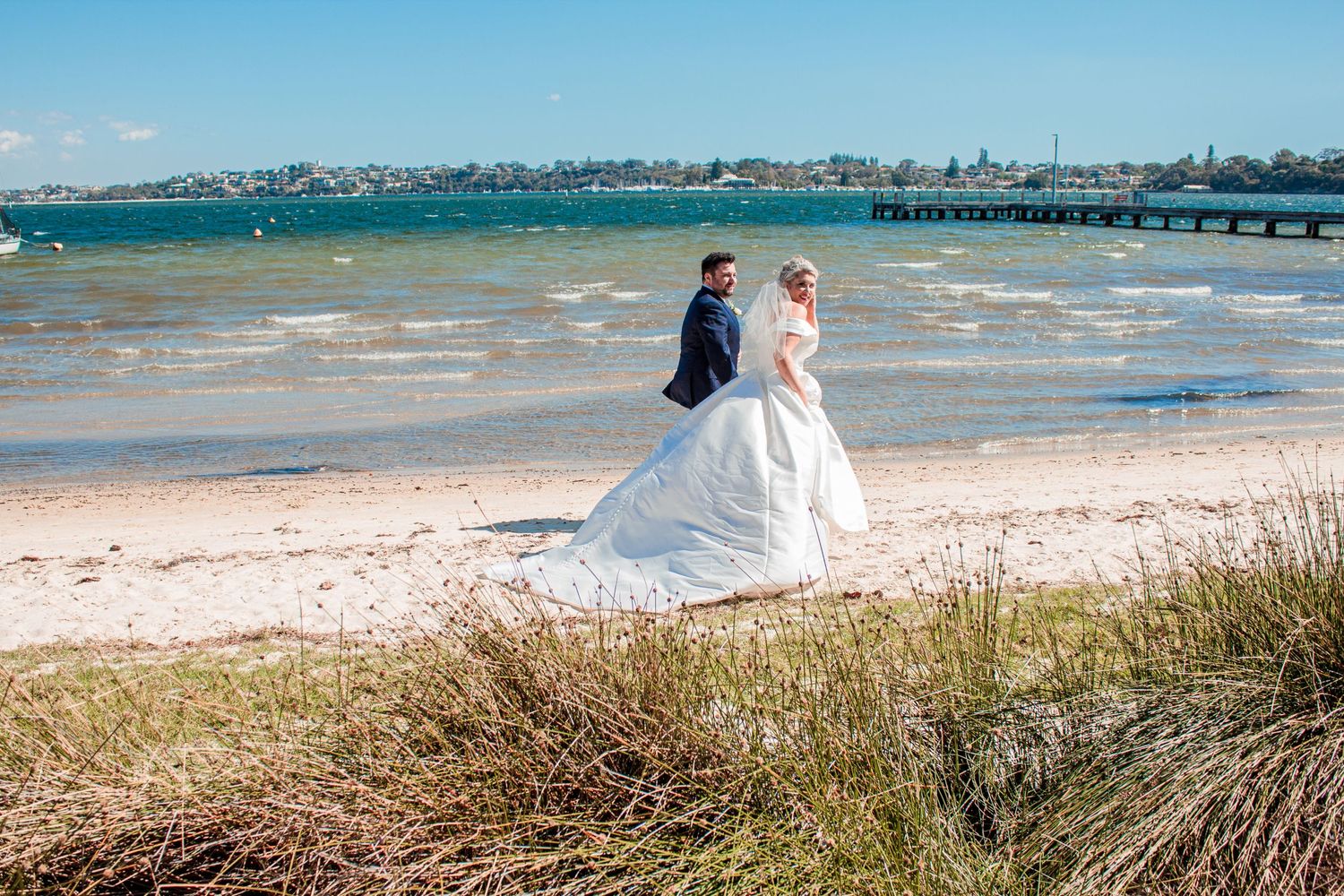 Wedding couple standing on beach with turquoise water and mountains in background.