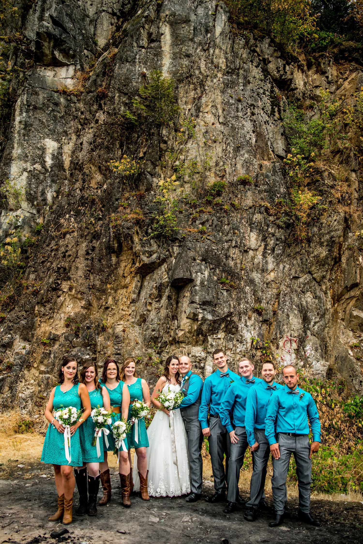 Wedding party in turquoise and white poses against dramatic rock cliff backdrop.