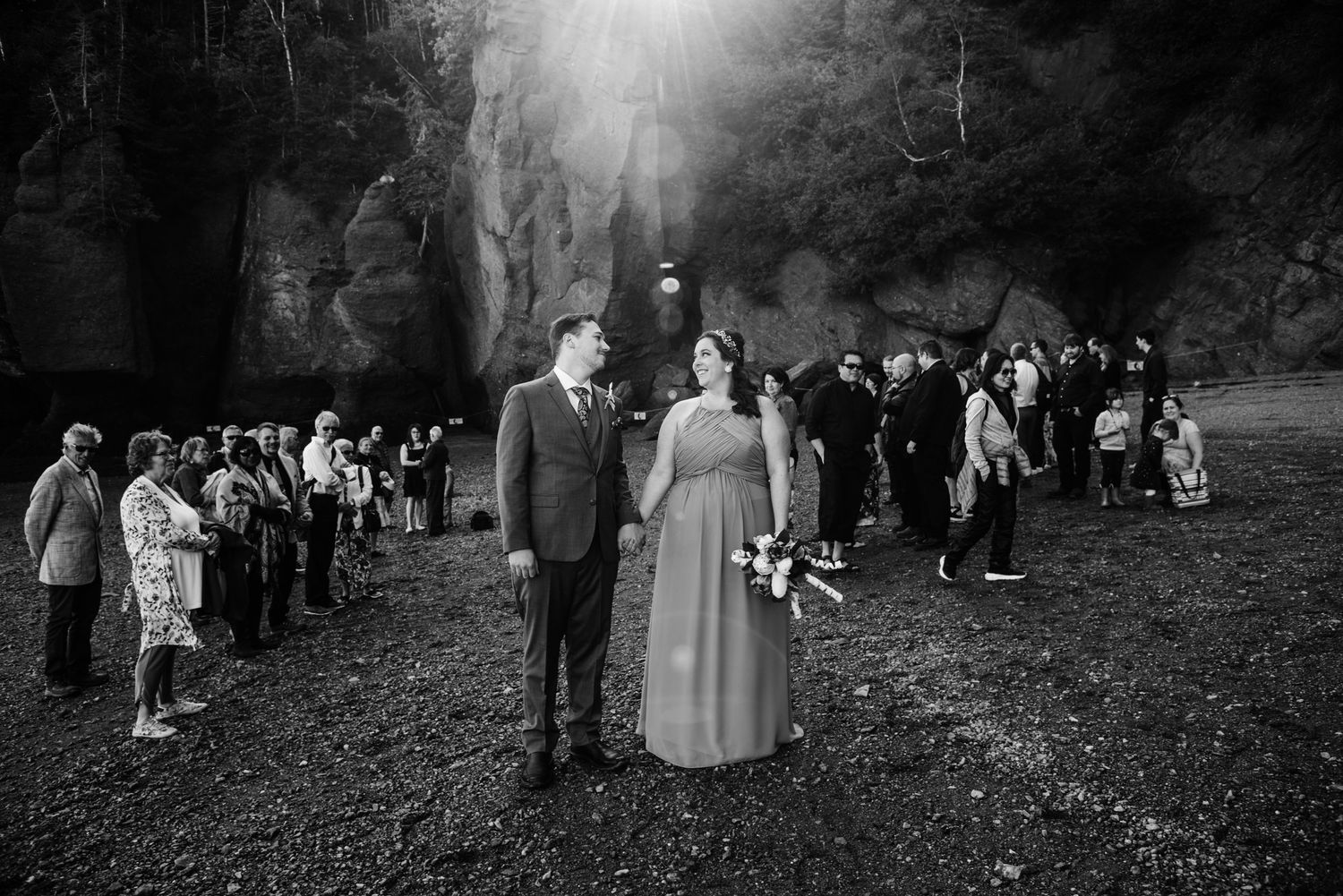 Black and white wedding photo with guests gathered in a wooded outdoor setting.