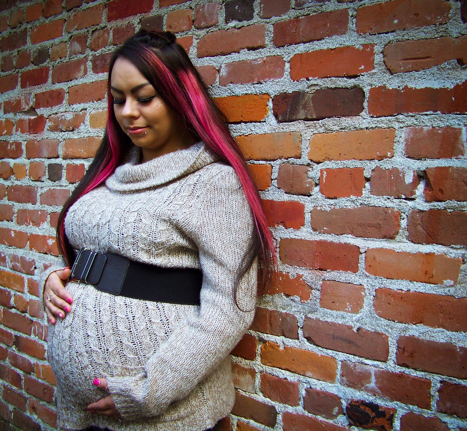 Pregnant mother cradling belly in front of brick during an outdoor maternity photography session taken by Tina Marie.