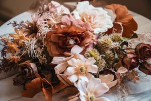 Romantic autumn-toned floral arrangement with blush and copper colored blooms on a light surface.
