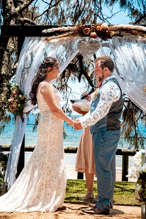 Beachside wedding ceremony setup with flowing white curtains and ocean views in the background.