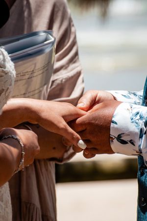 Close-up of hands exchanging something during an outdoor ceremony.
