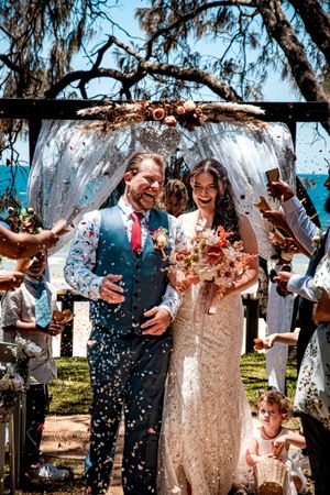 Joyful celebration with confetti being thrown at a beachside wedding under trees.