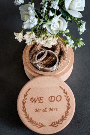 Wedding rings nestled in wooden ring box with white floral decorations.