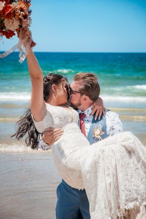 Romantic beach wedding portrait with waves and blue sky in the background.