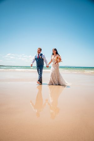 Couple walking along pristine sandy beach with clear blue skies and ocean waves.