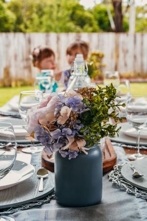 Elegant table setting with blue vases holding purple hydrangeas and greenery on gray tablecloth.