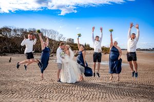 Wedding party jumping joyfully on beach with blue sky background.