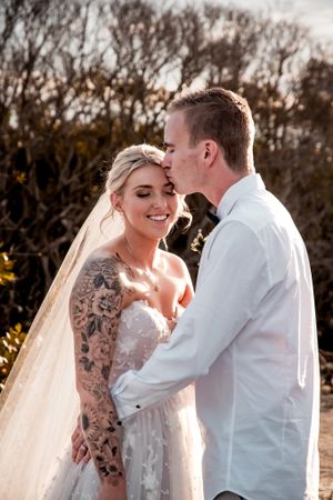 Romantic sunset wedding photos on beach with couple in white attire.