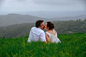 Couple sitting together in green field with misty mountains in background.