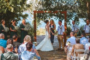 Outdoor wedding ceremony under a wooden arch decorated with flowers overlooking a scenic landscape.