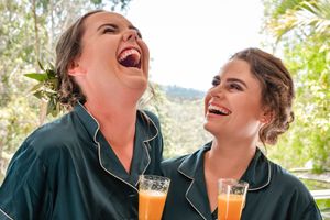 Two people in green pajamas sharing a laugh while holding mimosa glasses.